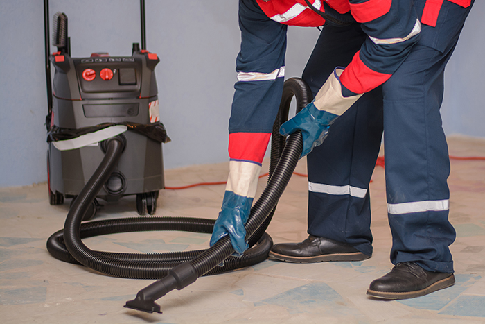 Man Vacuuming a Construction Site. Closeup of a cleaner in special clothes and rubber gloves holds a brush from an industrial professionally vacuum cleaner; Shutterstock ID 1077863696; purchase_order: PRE-ELEC PP 18873; job: ; client: ; other: